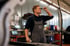 Mechaniker in grauer Mazda-Uniform inspiziert Motorraum mit Werkzeug.