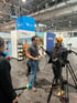 Ein Mann wird vor einer Kamera und mit Mikrofon auf einer Messe am Stand von allive und ikk classic interviewt.
