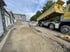 Gelber LKW mit angehobener Mulde auf einer Baustelle neben einem Schotterweg und Steingebäuden.