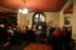 Mann steht vor Gruppe von Menschen in einem Restaurant mit roter Decke und Kronleuchter.