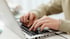 Hände tippen auf der Tastatur eines silbernen Laptops.