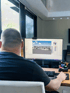 Ein Mann sitzt an einem Schreibtisch vor einem Monitor, auf dem eine 3D-Architekturzeichnung mit dem Text „GT“ und Gebäudemodell zu sehen ist.