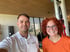 Ein lächelnder Fitnesstrainer im weißen Poloshirt und eine rothaarige Frau in einem hellen Fitnessstudio.