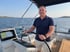 Mann in blauem Poloshirt und Shorts steuert eine Bavaria C46 Segelyacht auf dem Meer.