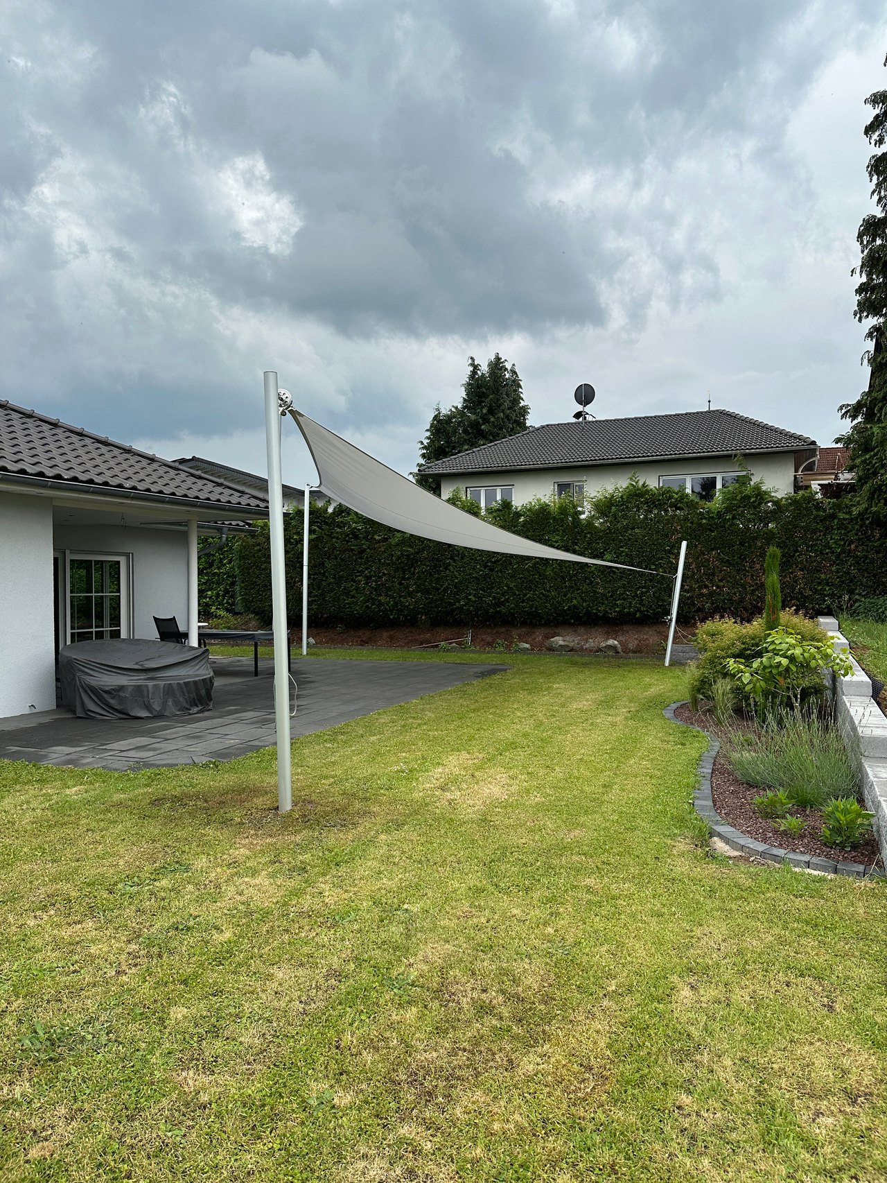 Weißes Dreieckssegel am Mast über einer großen Rasenfläche im Garten