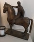 Bronzeskulptur eines Reiters auf einem Pferd, daneben ein Kerzenhalter mit weißer Kerze.