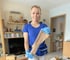 Eine lächelnde Frau in blauem T-Shirt und hellblauen Handschuhen hält einen hautfarbenen Kompressionsstrumpf.