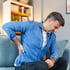 Man on sofa holding lower back, showing sciatica pinched nerve pain.