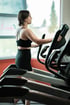 Eine Frau in schwarzer Sportkleidung trainiert auf einem Ellipsentrainer im Fitnessstudio.