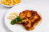Zwei goldbraun panierte Schnitzel mit Zitronenscheiben und Petersilie auf einem Teller neben einer Schale Pommes frites.