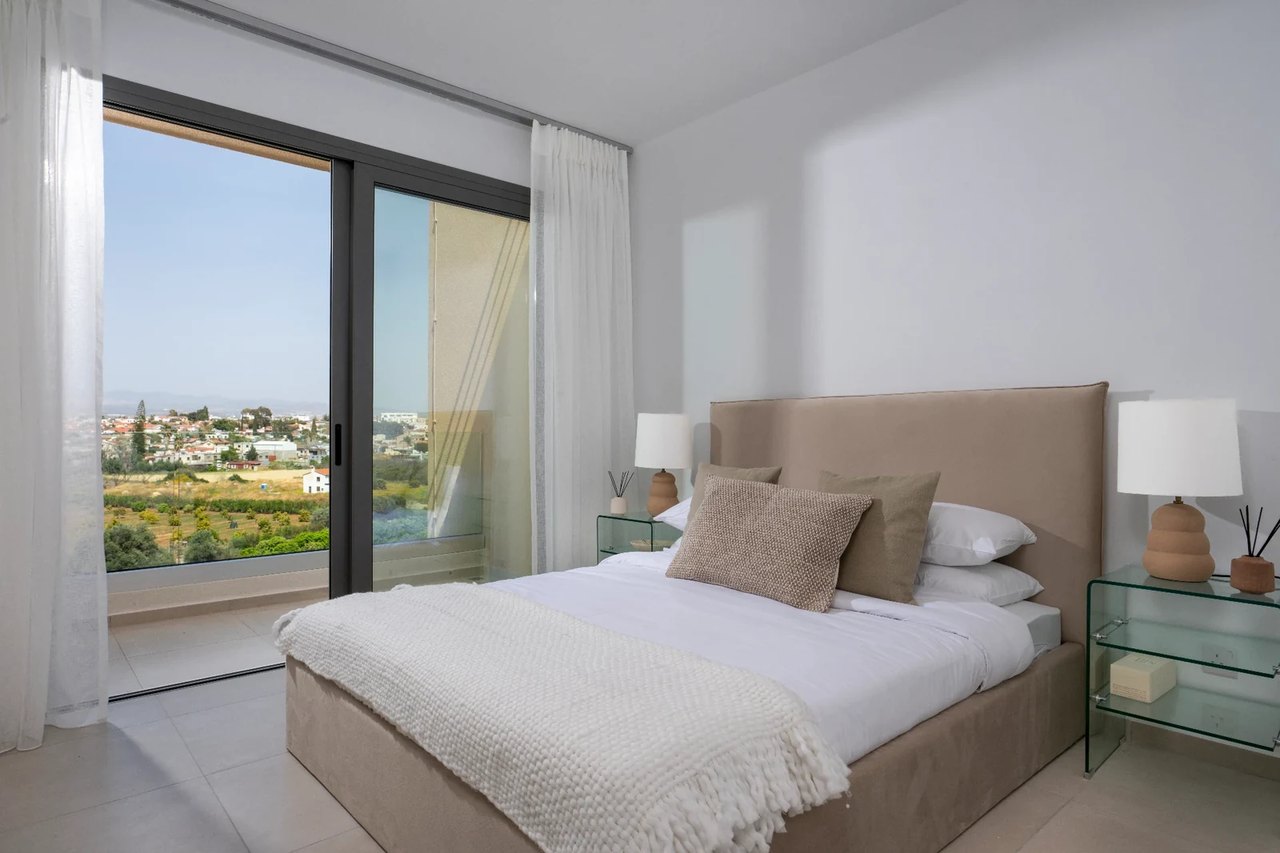 Schlafzimmer in Limassol mit Doppelbett und Blick durch eine große Glasfront nach draußen.