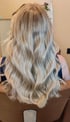 Rückansicht einer Person mit langen, gewellten Haaren in kühlem Blond und Balayage-Optik in einem Friseursalon.