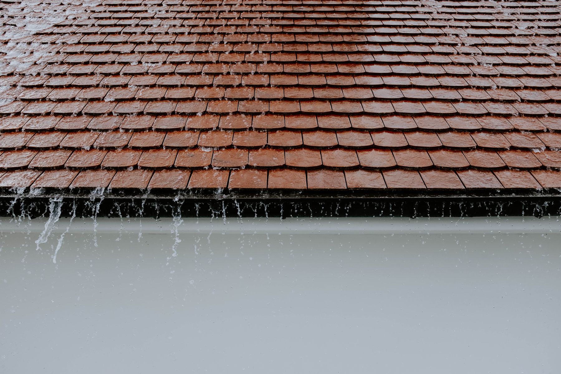 Heavy rainwater running down a sloped shingle roof
