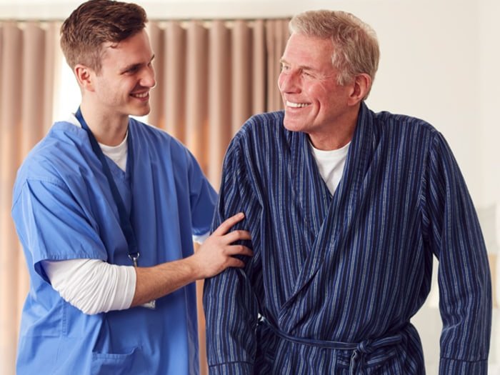Pfleger unterstützt einen Senior beim Gehen mit dem Rollator