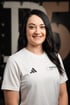 Lächelnde Frau mit langen dunklen Haaren im weißen Adidas-T-Shirt mit dem Logo Therapier This Is Physio und Pier5 