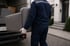 Umzugshelfer in blauer Uniform trägt graues Sofa aus einem Lastwagen.