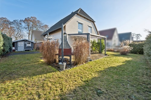 Garten mit Rasen, Grill und Schuppen neben einem Haus mit Pergola.