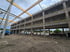 Ein mehrstöckiger Rohbau aus Beton mit Holzdeckenträgern auf einer Baustelle unter bewölktem Himmel.