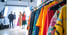 Bunte Kleidung hängt im Vordergrund, unscharfe Models posieren im Hintergrund vor Studiobeleuchtung.