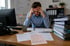 Gestresster Mann am Schreibtisch mit Händen am Kopf, umgeben von Papieren und Aktenordnern im Büro - Software-KRITIS Notfall- und Krisenmanager (NKM®).