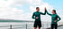 Man and woman in athletic wear giving each other a high-five by a lake under a cloudy sky.