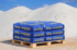 Blaue Säcke mit "25 kg trendyQUARZ" auf einer Holzpalette vor Sandhügeln.