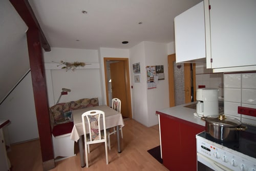 Küche mit Essecke, Holzbalken, roter Arbeitsplatte, weißen Schränken und Kaffeemaschine.