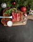 Geschnittenes Steak auf Holzbrett mit Rosmarin, Knoblauch, Pfefferkörnern, Salz und Weihnachtsdekoration.