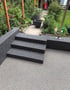 Eine Terrasse mit grauen Granittreppen führt zu einem Gartenweg mit Pflanzen und einem roten Spielgerätschlitten.