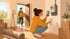 Frau fotografiert Smart Meter mit Smartphone, Mann trägt Umzugskarton durch offene Tür.