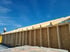 Zwei Bauarbeiter auf einem Holzrahmenhaus mit blattförmigen Dachsparren unter blauem Himmel.