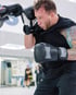 Tätowierter Mann beim Boxtraining mit schwarzen Boxhandschuhen in einer Deckungshaltung im Boxstudio.