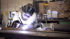 Ein Schweißer mit Schutzhelm und Handschuhen schweißt ein Metallstück mit hellen Funken in einer Werkstatt.