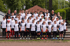 Eine große Gruppe von jungen Fußballspielern und erwachsenen Trainern posiert auf Tribünenstufen für ein Gruppenfoto.