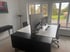 Heller Arbeitsplatz mit weißem Schreibtisch, Monitor und schwarzem Sideboard, durch die Fenster Blick in den Garten