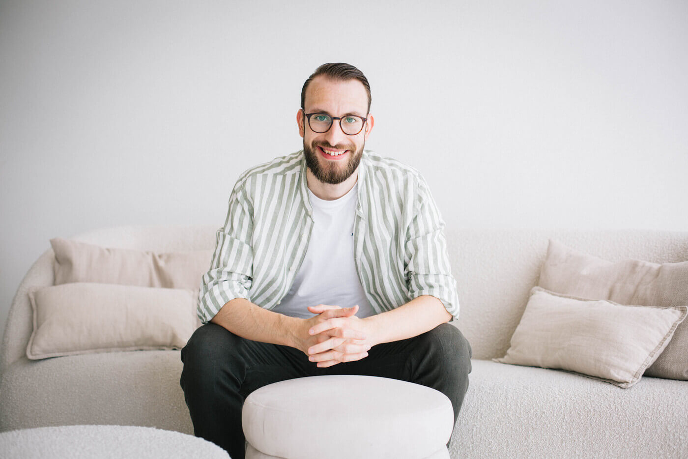 Erik Rulands sitzt auf einem hellen Sofa, die Hände gefaltet, und blickt in die Kamera