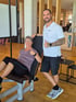 Ein Fitnesstrainer und eine Kundin geben an einem Trainingsgerät lächelnd ein Daumen-hoch-Zeichen im Fitnessstudio.