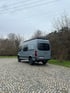 Heckansicht eines ausgebauten Mercedes Sprinter Reisewagens mit festem Hochdach – kompakter Reisewagen auf Parkplatz vor bewaldeter Kulisse