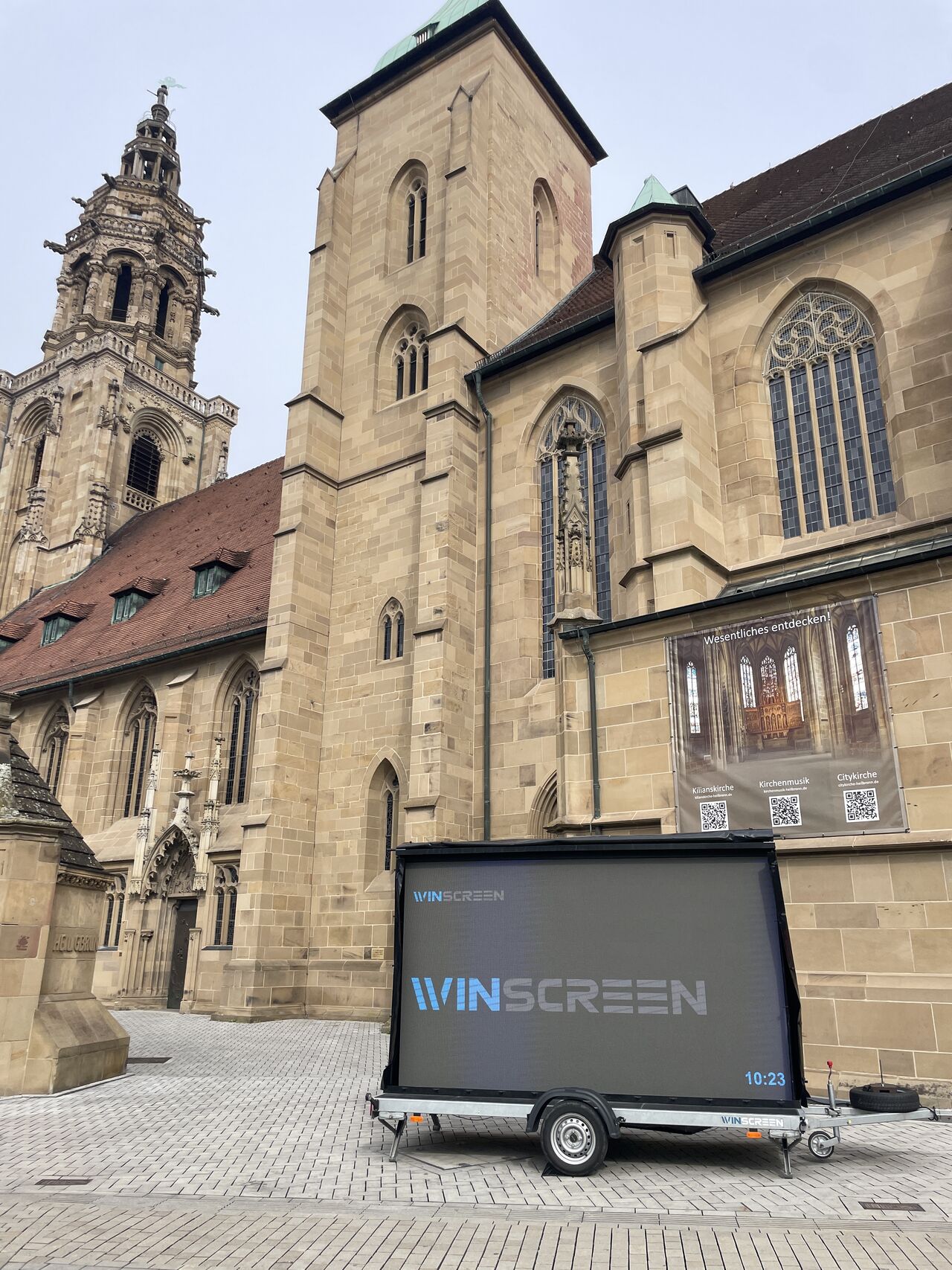 Zwei Monteure setzen auf einer Hebebühne LED-Module in den Stahlrahmen einer Werbeanlage an einer Hallenfassade ein