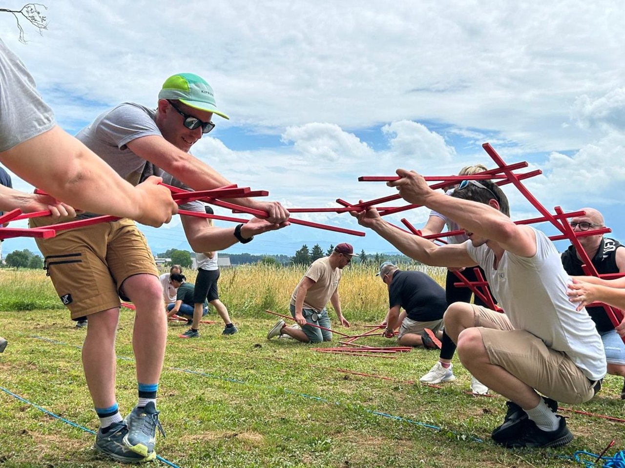 Team löst gemeinsam eine Aufgabe mit roten Holzstäben auf einer Wiese