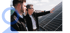 Zwei Männer betrachten Solarpaneele auf einem Dach, einer zeigt darauf.