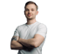 Ein lächelnder Mann in einem weißen T-Shirt mit verschränkten Armen vor grünem Hintergrund.