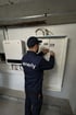 Techniker mit "enerly"-Logo auf dem Rücken, der an einem Sicherungskasten in der Nähe eines Wechselrichters arbeitet.