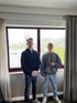 Zwei junge Männer stehen vor einem Fenster mit Blick auf den Kölner Dom, die Hohenzollernbrücke und den Rhein.