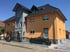 Zweigeschossiges Haus mit oranger und grauer Fassade, schwarzem Dach, schwarzem Zaun und gepflasterter Einfahrt.