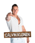 Calvin Kleinen lächelt und zeigt mit dem Finger nach vorne, vor einem Holzschild mit seinem Namen.
