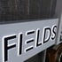 Leuchtende Buchstaben "FIELDS" auf einem weißen Schild mit schwarzem Hintergrund.