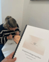 Eine Person hält ein Heft mit dem Titel "Wimpernverlängerung Basic" während eine andere Person an einem Übungskopf arbeitet.