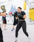 Lächelnde Frau beim Boxtraining mit schwarzen Boxhandschuhen im Boxclub BACKYARD mit gelben Boxsäcken.
