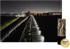 Nachtansicht einer beleuchteten Eisenbahnstrecke mit einem Industriekomplex im Hintergrund.